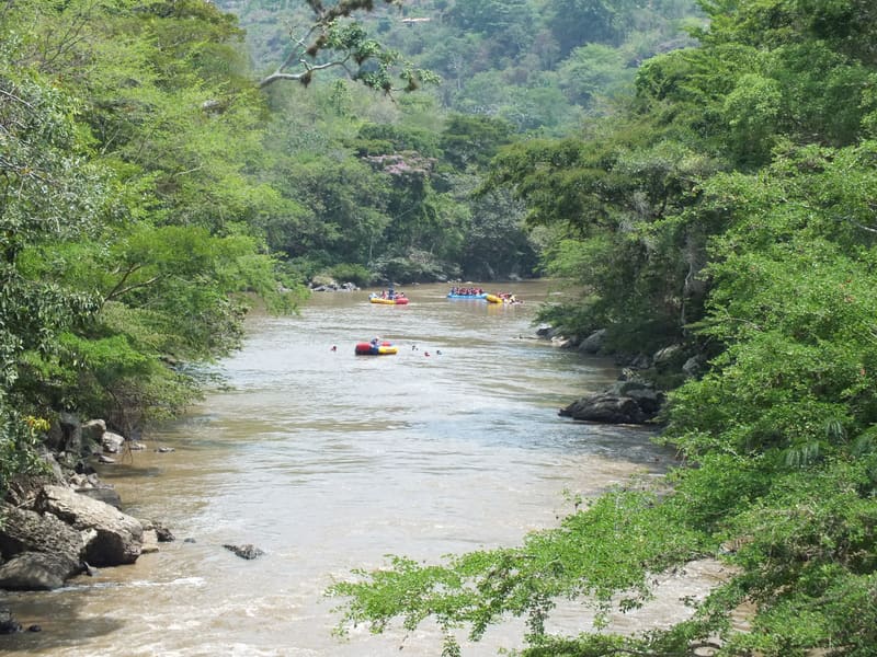 El río Fonce corre entre árboles; a lo lejos se ven balsas de rafting.